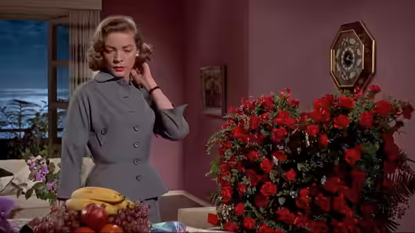 Lucy Moore Hadley (Lauren Bacall) stands beside a table and a large arrangement of roses