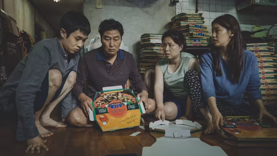 Four people kneeling around an open pizza box on the floor