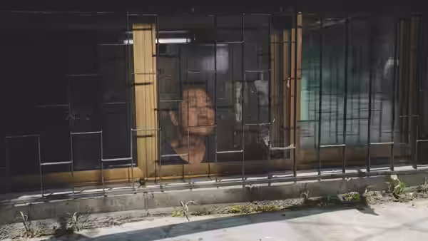 Man peering out through the bars of a basement window