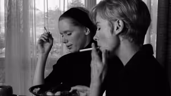 A woman and a man sit by a window, smoking