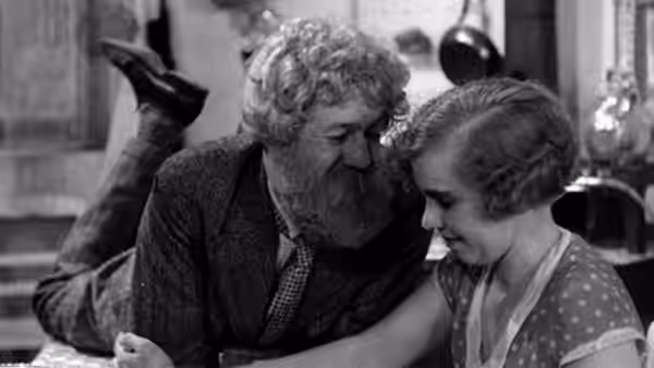 Boudu (Michel Simon) leans close to a woman seated beside him at a table