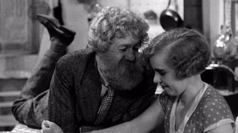 Boudu (Michel Simon) leans close to a woman seated beside him at a table