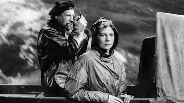 A man adjusts Joan Webster's (Wendy Hiller) hood aboard a boat