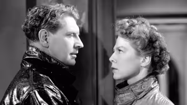 Torquil MacNeil (Roger Livesey) and Joan Webster (Wendy Hiller) face each other indoors