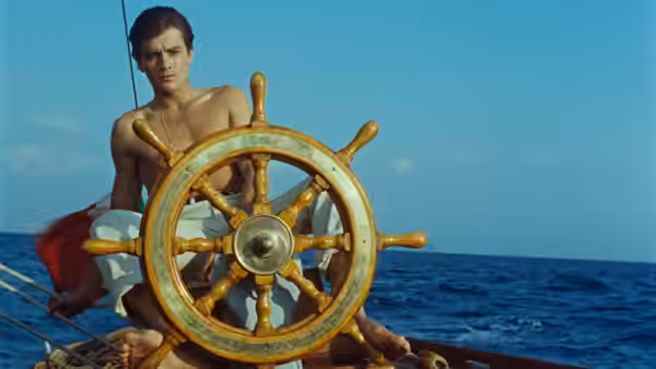 Tom Ripley (Alain Delon) grips a ship's wheel against the open sea