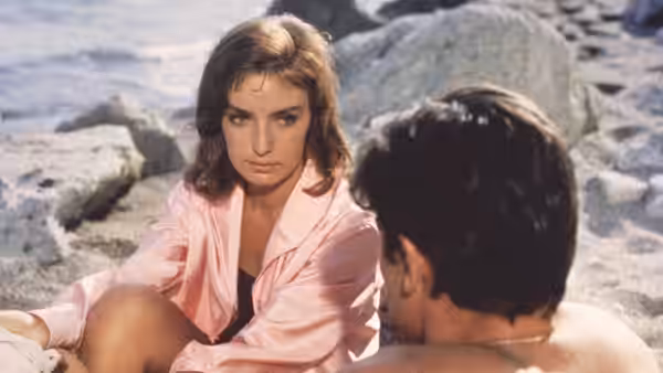 Marge Duval (Marie Laforêt) sits among seaside rocks facing a man