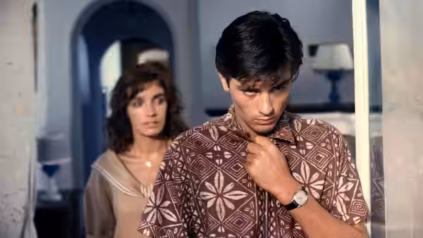 Tom Ripley (Alain Delon) adjusts his shirt as Marge Duval watches from behind