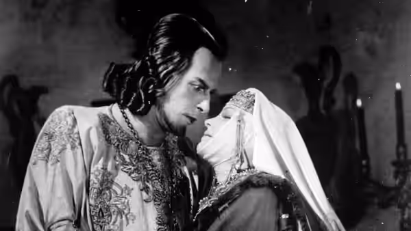 A richly dressed man leans close to a veiled woman indoors