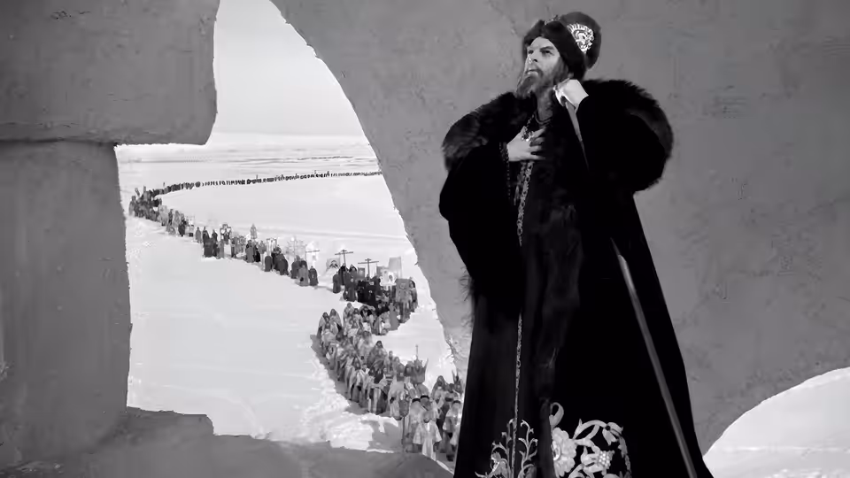 Ivan stands by a window overlooking a procession winding through the snowy landscape
