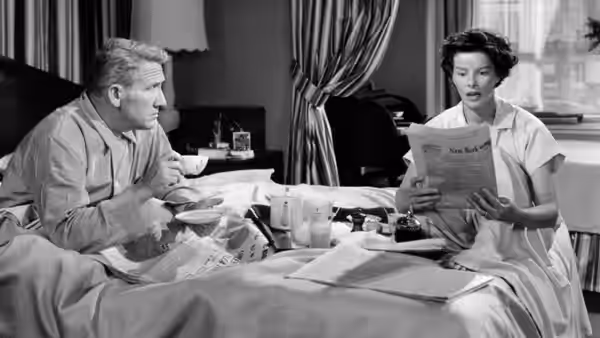 Adam Bonner (Spencer Tracy) sits in bed as Amanda Bonner (Katharine Hepburn) holds up a document