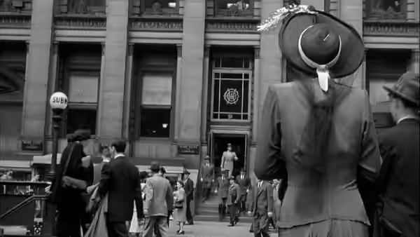 A woman in a wide-brimmed hat watches people enter a courthouse