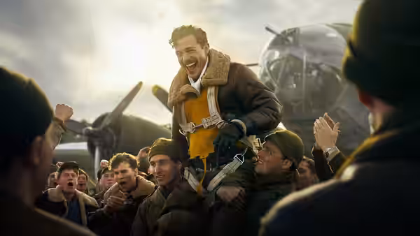 Airmen lift a grinning officer in flight gear above a cheering crowd