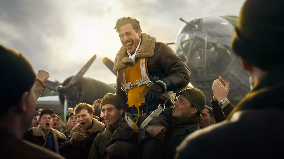 Airmen lift a grinning officer in flight gear above a cheering crowd