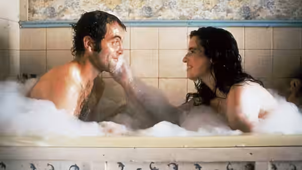 A man and woman share a foamy bath in a tiled bathroom