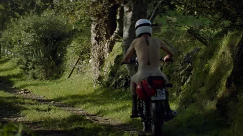 A helmeted man rides a motorcycle along a wooded country lane