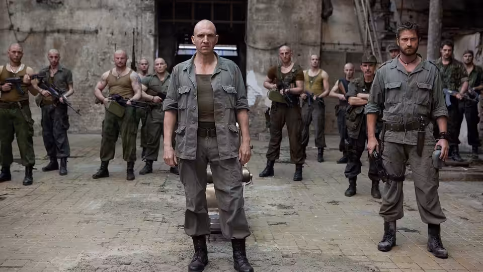 Coriolanus (Ralph Fiennes) stands with armed soldiers in a ruined hall, Aufidius (Gerard Butler) beside him