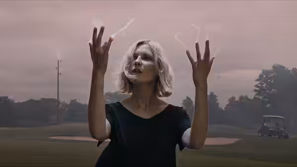 Justine (Kirsten Dunst) raising smoking hands on a misty golf course