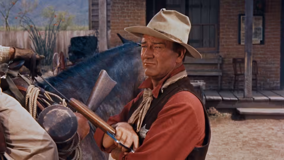 Sheriff Chance (John Wayne) holding a rifle beside a horse