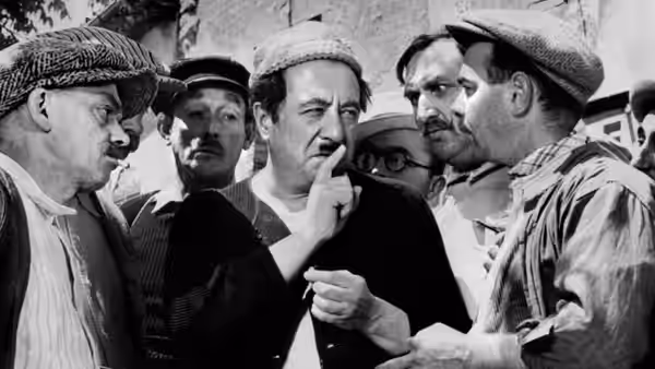 Aimable Castanier (Raimu) listens as several villagers crowd around him outdoors