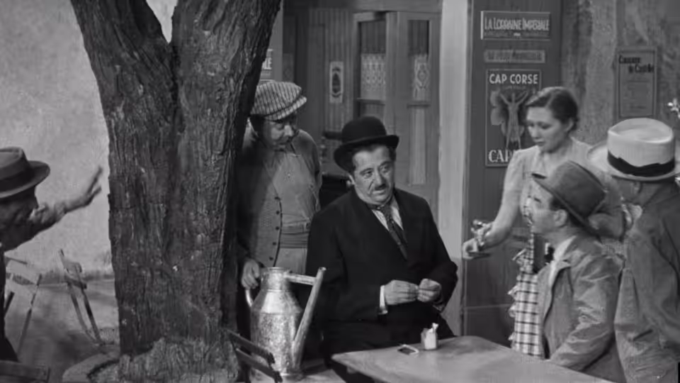 Aimable Castanier (Raimu) sits at a table in the bakery as villagers gather around him