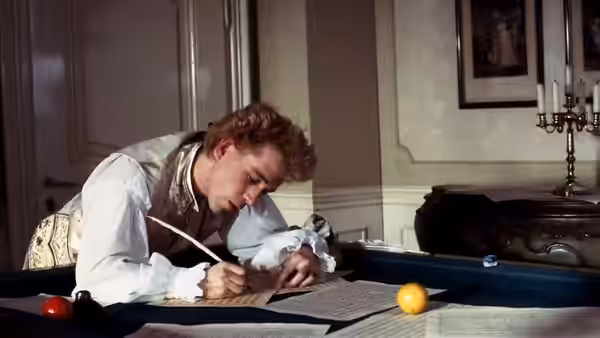 Mozart (Tom Hulce) writing music at a billiard table in daylight