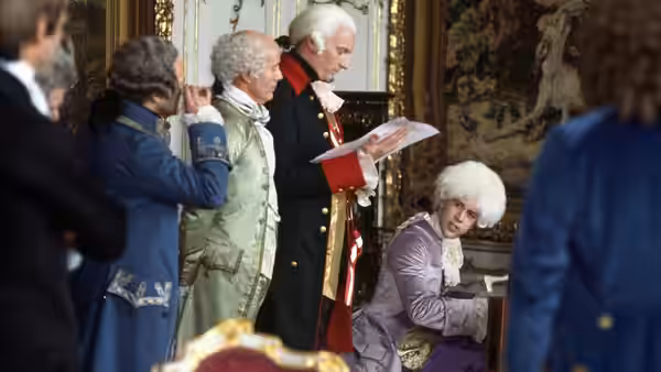 Wigged courtiers stand examining papers in a gilded formal chamber