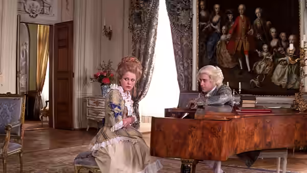 A woman in a gown listens to a man playing piano in a salon