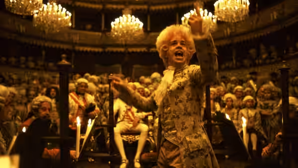 Mozart (Tom Hulce) raising both arms energetically before a theater audience