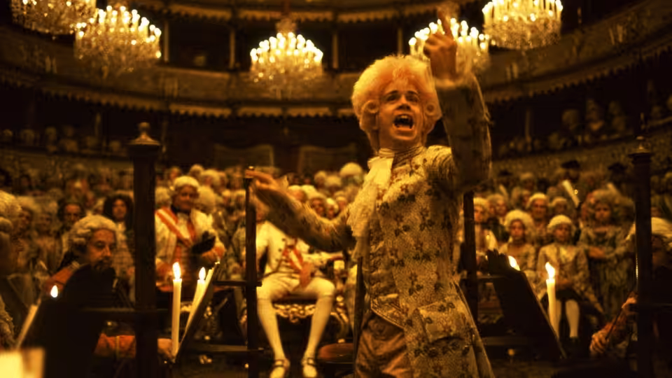 Mozart (Tom Hulce) raising both arms energetically before a theater audience