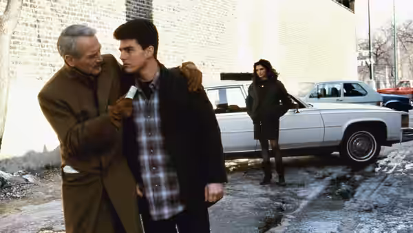 Eddie Felson (Paul Newman) walks with Vincent Lauria (Tom Cruise) beside a parked car as Carmen follows