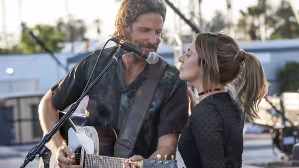 Jackson Maine (Bradley Cooper) sings into microphone with Ally (Lady Gaga) nearby
