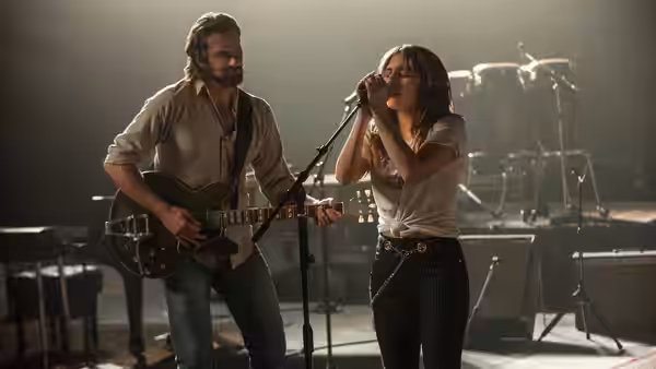 Jackson Maine (Bradley Cooper) plays guitar as Ally (Lady Gaga) sings onstage