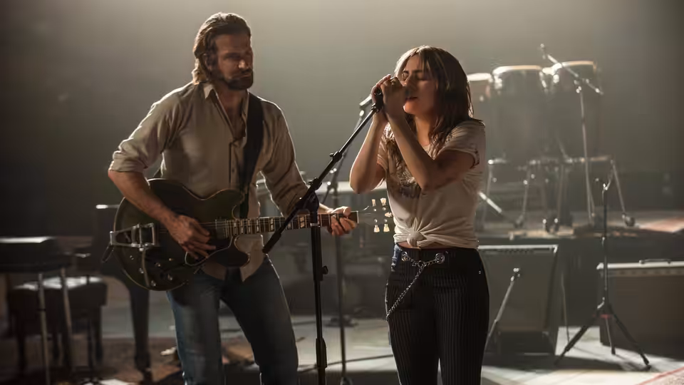 Jackson Maine (Bradley Cooper) plays guitar as Ally (Lady Gaga) sings onstage