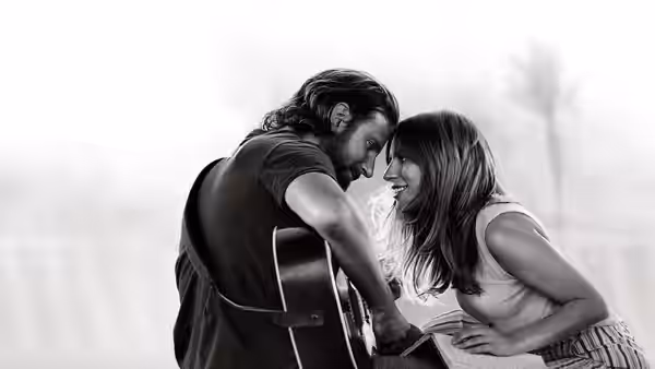 Jackson Maine (Bradley Cooper) holds guitar beside smiling Ally (Lady Gaga) outdoors
