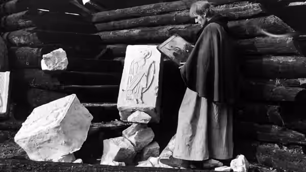 A robed monk studies an icon among carved stone blocks