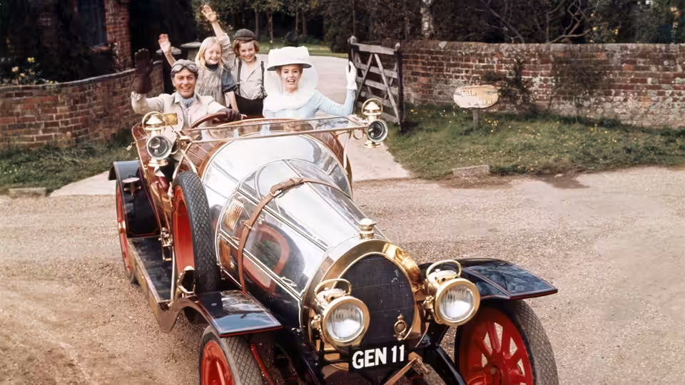 Family waving from an open polished vintage automobile on a country lane