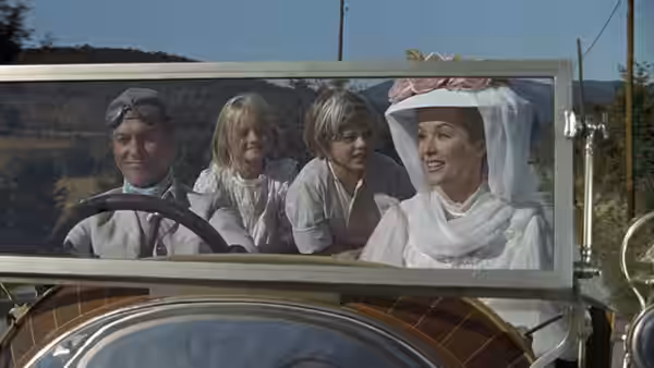 Driver and passengers seated inside a vintage car on a rural road
