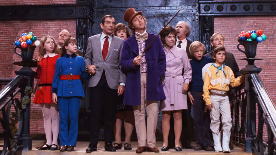 Willy Wonka (Gene Wilder) stands with children and adults on a staircase