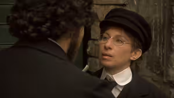 Yentl, dressed as a young man, speaks with a bearded man beside a doorway