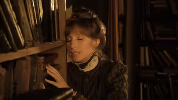 Yentl reaches for a book on a crowded library shelf