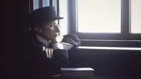 Yentl, dressed as a young man, rests by a bright window
