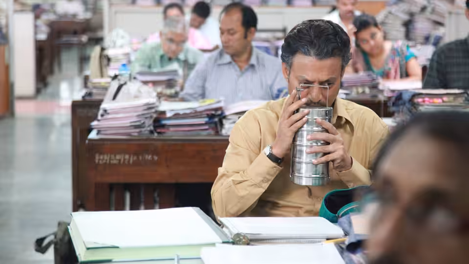 Saajan Fernandes (Irrfan Khan) drinks from a metal lunchbox at his crowded office desk