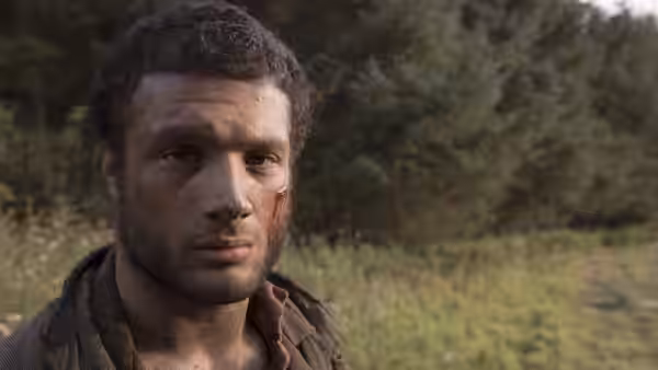 Sebastian (Cosmo Jarvis), with a cut on his cheek, stands in a wooded clearing
