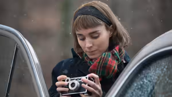 Therese Belivet (Rooney Mara) examining a camera while standing in falling snow