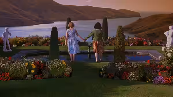 two young women holding hands in a landscaped garden overlooking water