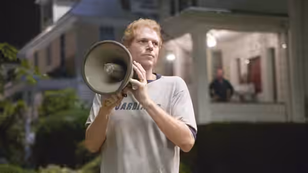 A man with a megaphone stands outside a house at night