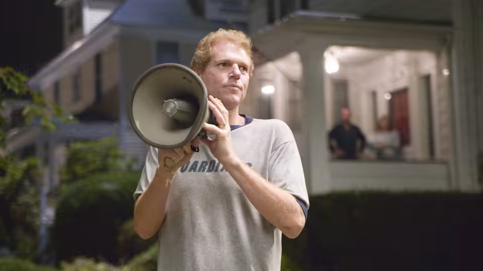 A man with a megaphone stands outside a house at night