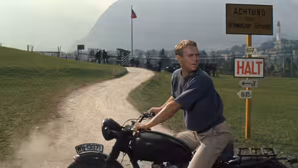 Hilts (Steve McQueen) riding a motorcycle past a border sign