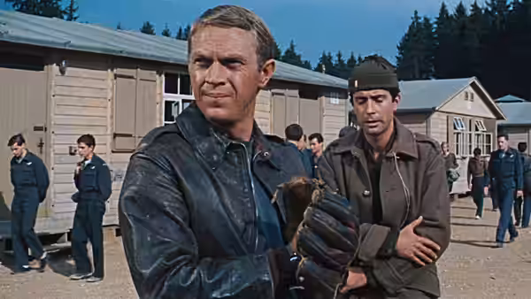 Hilts (Steve McQueen) standing with another man outside wooden barracks