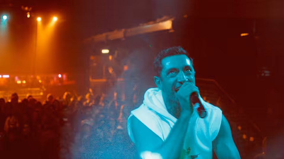 Zed (Riz Ahmed) raps into a microphone onstage before a crowd